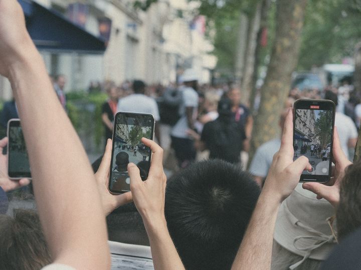 People on a busy street raise their phones to film a moment